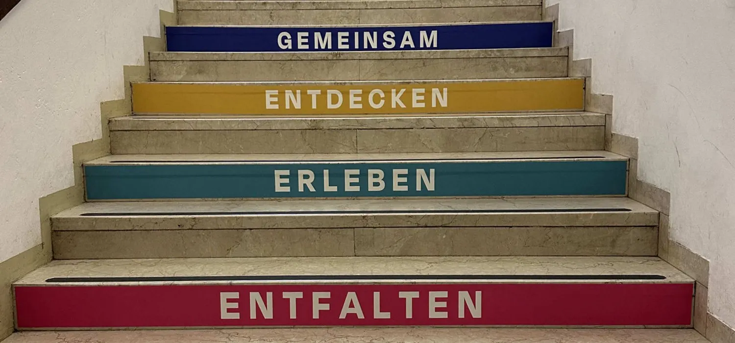 Die Treppe im MTG: Auf den Stufen stehen die Leitbegriffe Gemeinsam, Entdecken, Erleben und Entfalten in den Farben der Schule