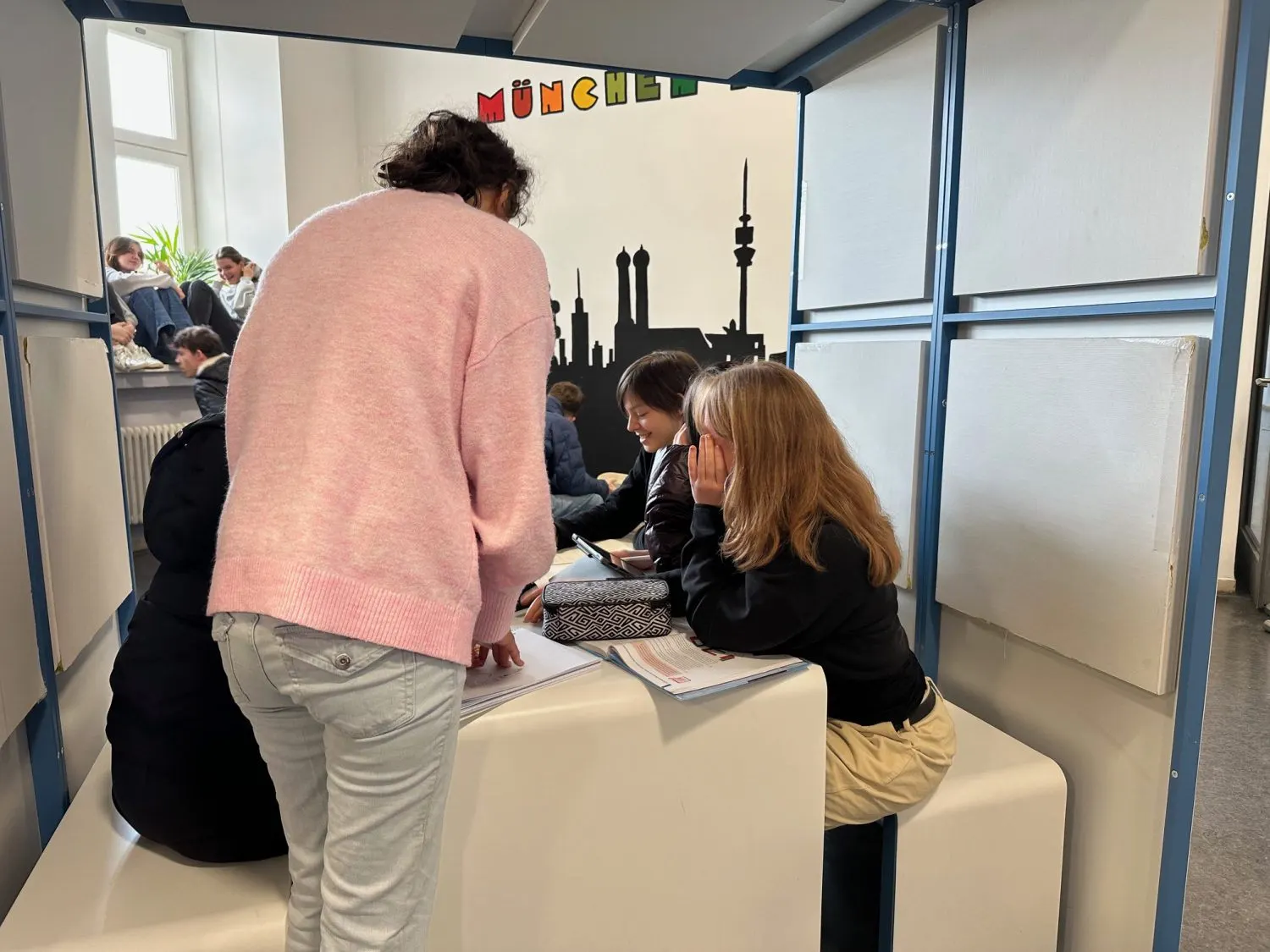 Zwei Schülerinnen arbeiten in der Lernlandschaft zusammen, an der Wand die Silhouette Münchens