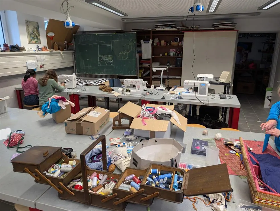 Nähwerkstatt mit Nähmaschinen, Stoffen und einer Box voller Garnrollen
