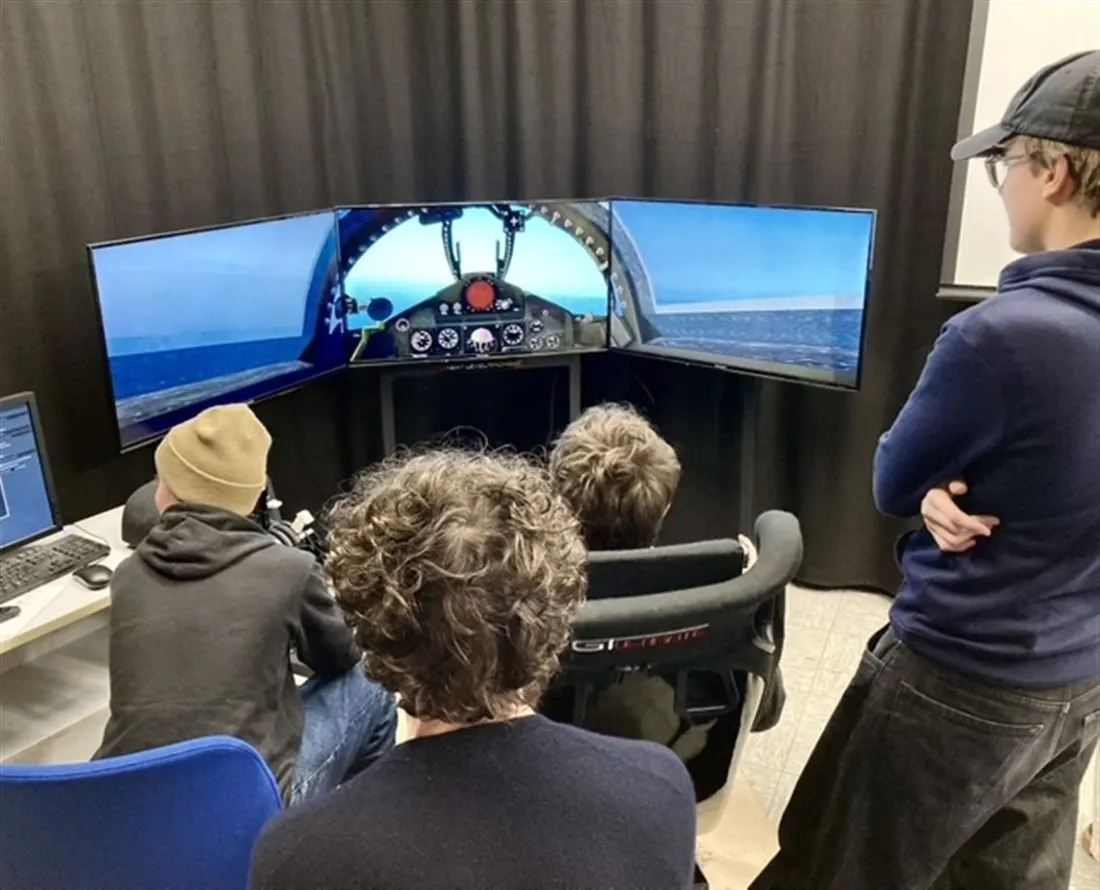 Schülerinnen und Schüler am Flugsimulator mit drei Bildschirmen