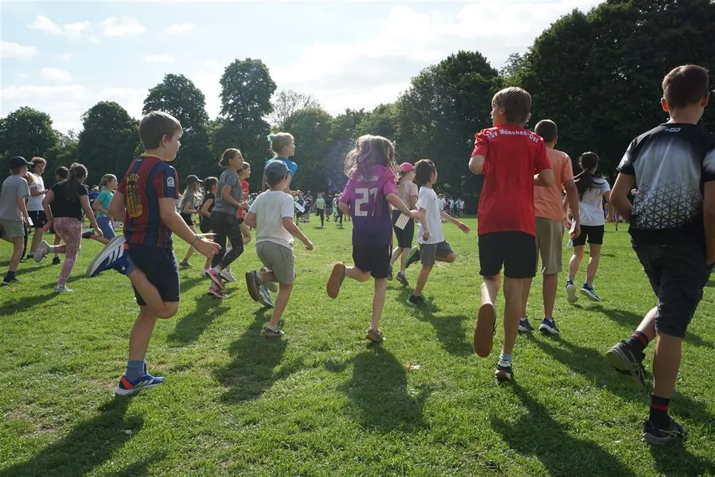 Schülerinnen und Schüler laufen bei sommerlichem Licht über die Wiese