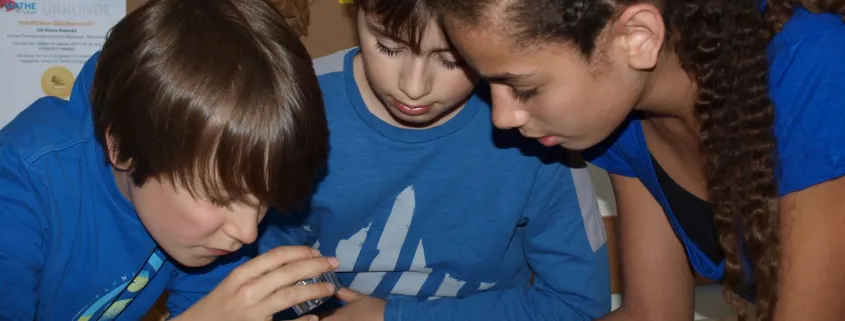 Drei Schülerinnen und Schüler beugen sich konzentriert über ein Objekt