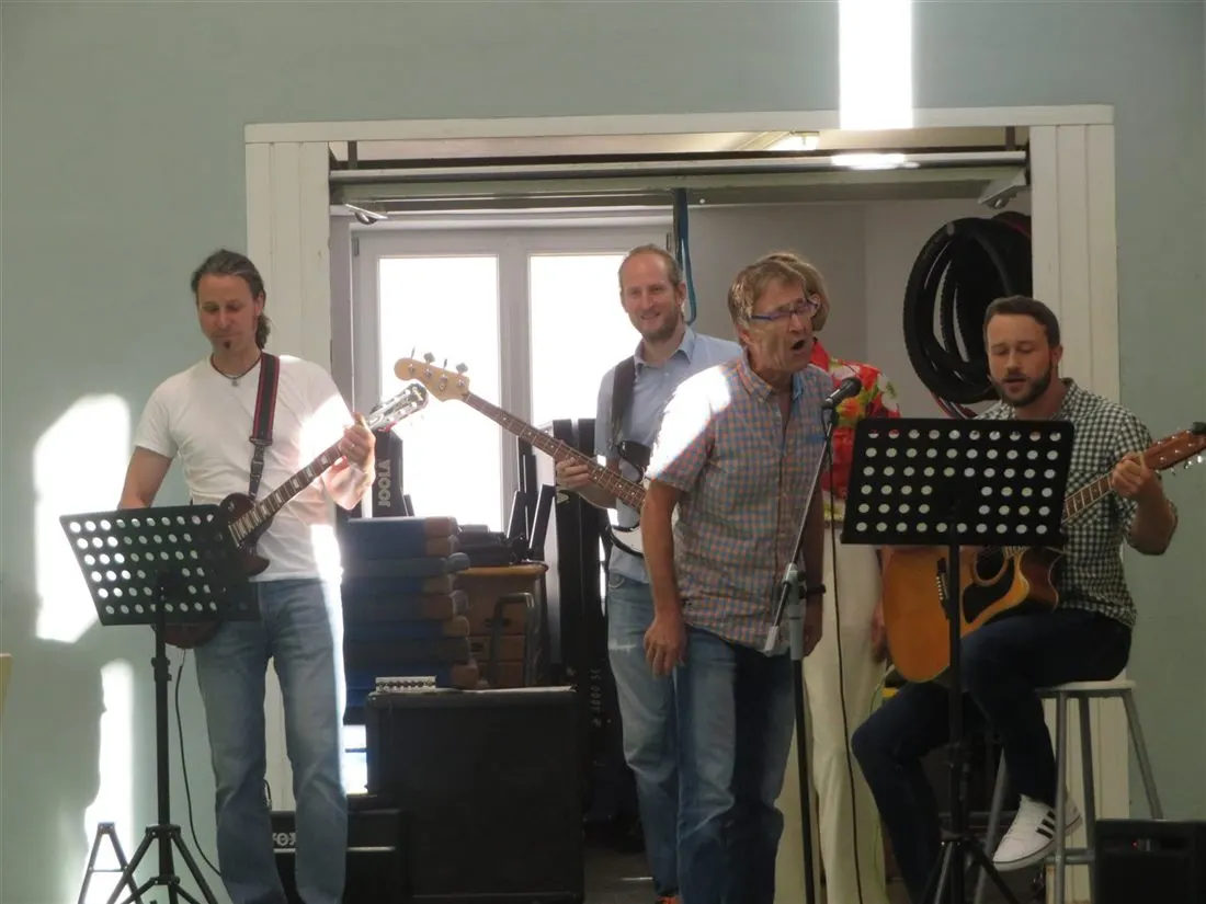 Fünf Lehrkräfte mit Gitarren, Bass und Mikrofon beim Auftritt in der Aula