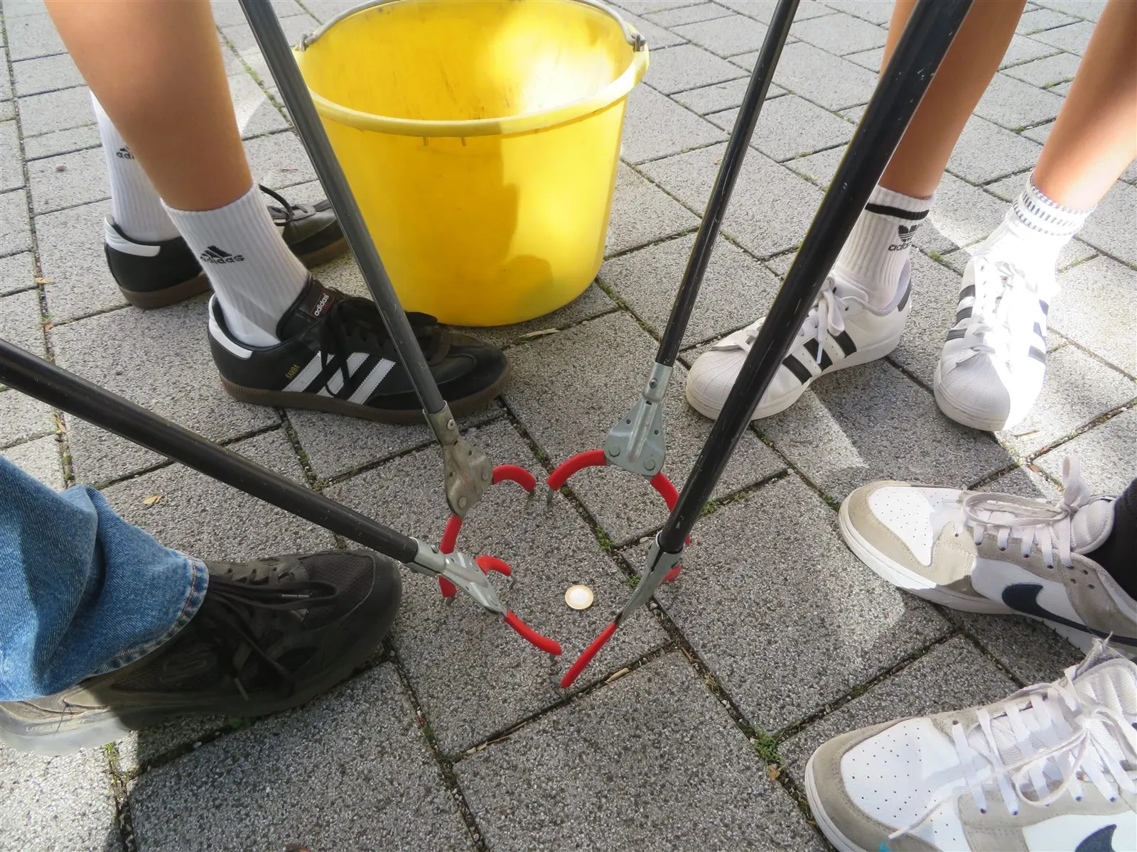 Vier Greifzangen bilden auf dem Pflaster ein Herz, ringsum die Schuhe der Beteiligten