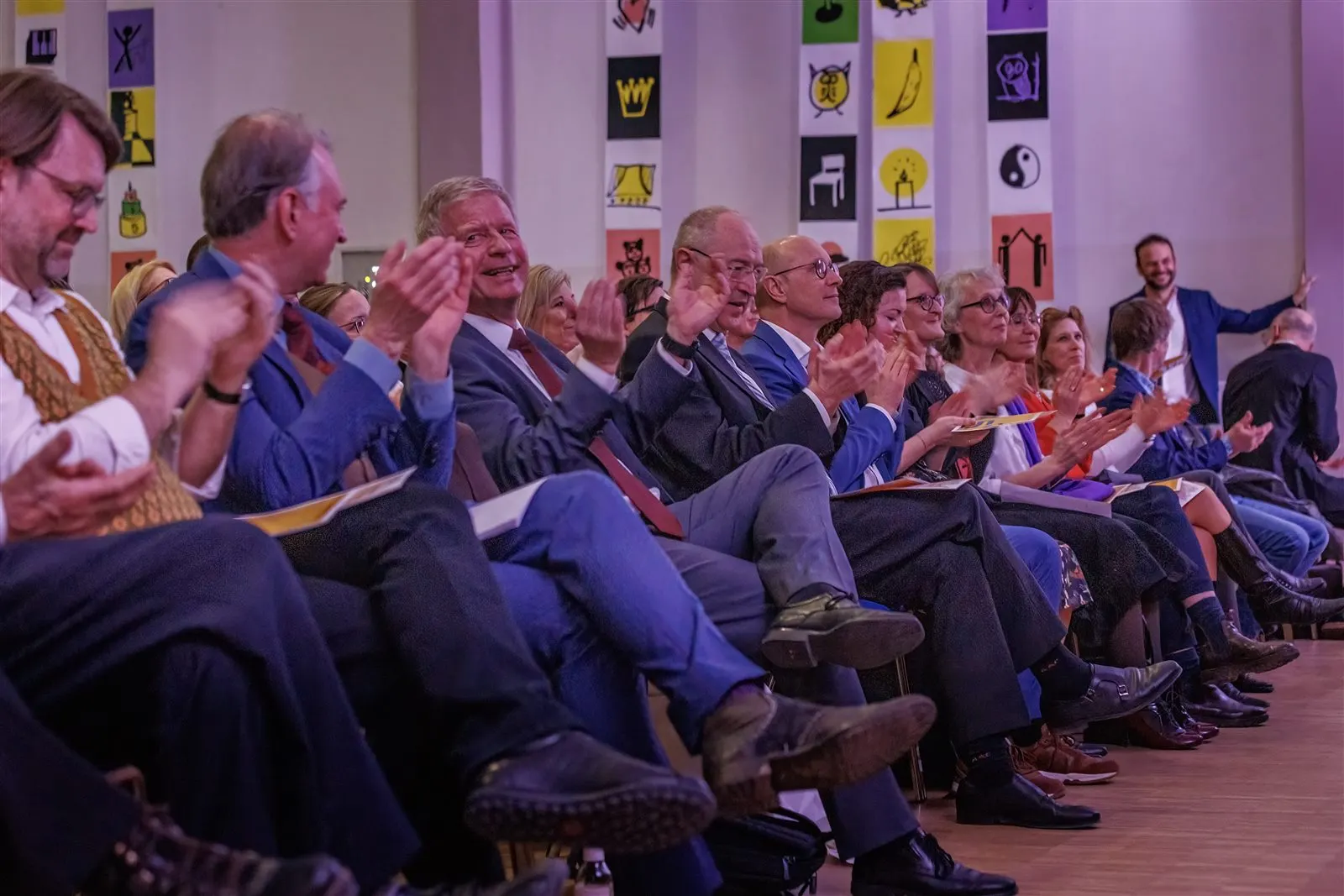 Begeisterte Gäste beim Festakt — bunte Wandbilder im Hintergrund