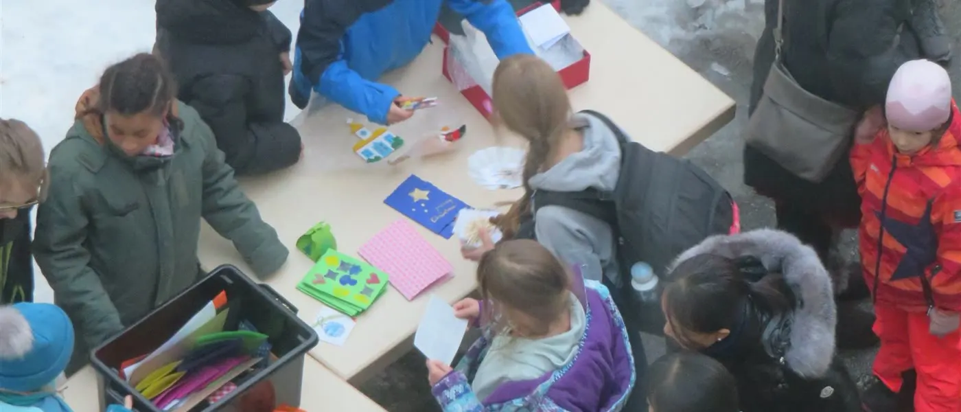 Adventsbasar im Pausenhof: Kinder in Winterjacken an einem Tisch mit selbstgebastelten Karten und Sternen